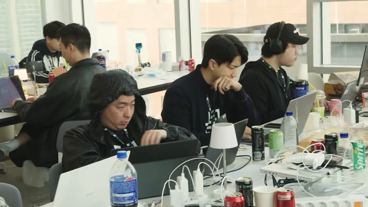 창가 테이블에 노트북을铺开한 채 몰입한 참가자들 — 책상 위의 음료·케이블이 장시간 작업을 보여준다